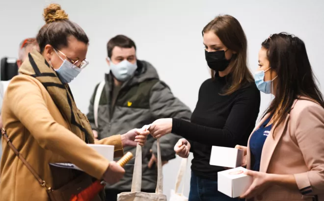 Een groep mensen met een mondmasker op die tote bags uitdelen