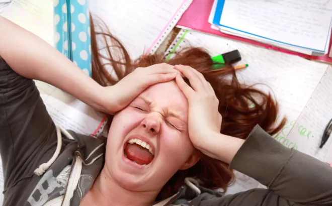 Une étudiante entourée de livres avec ses mains sur sa tête