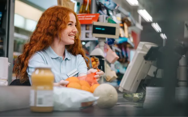 Een bijverdiener die lachend werkt achter de kassa van een supermarkt