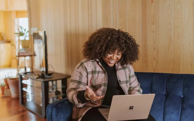 Jonge vrouw glimlacht terwijl ze naar het scherm van haar laptop kijkt